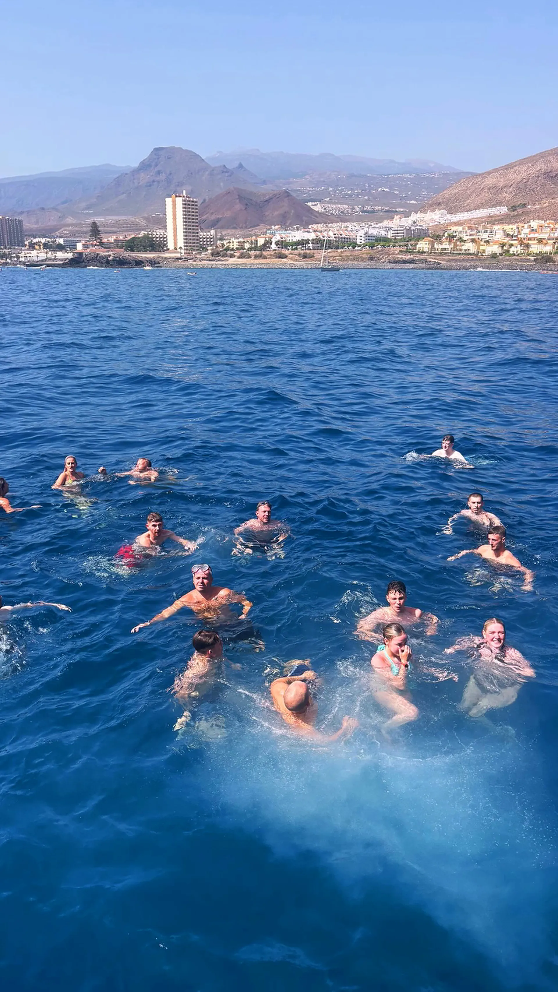 Group of guests swimming in clear blue ocean water near coastal town