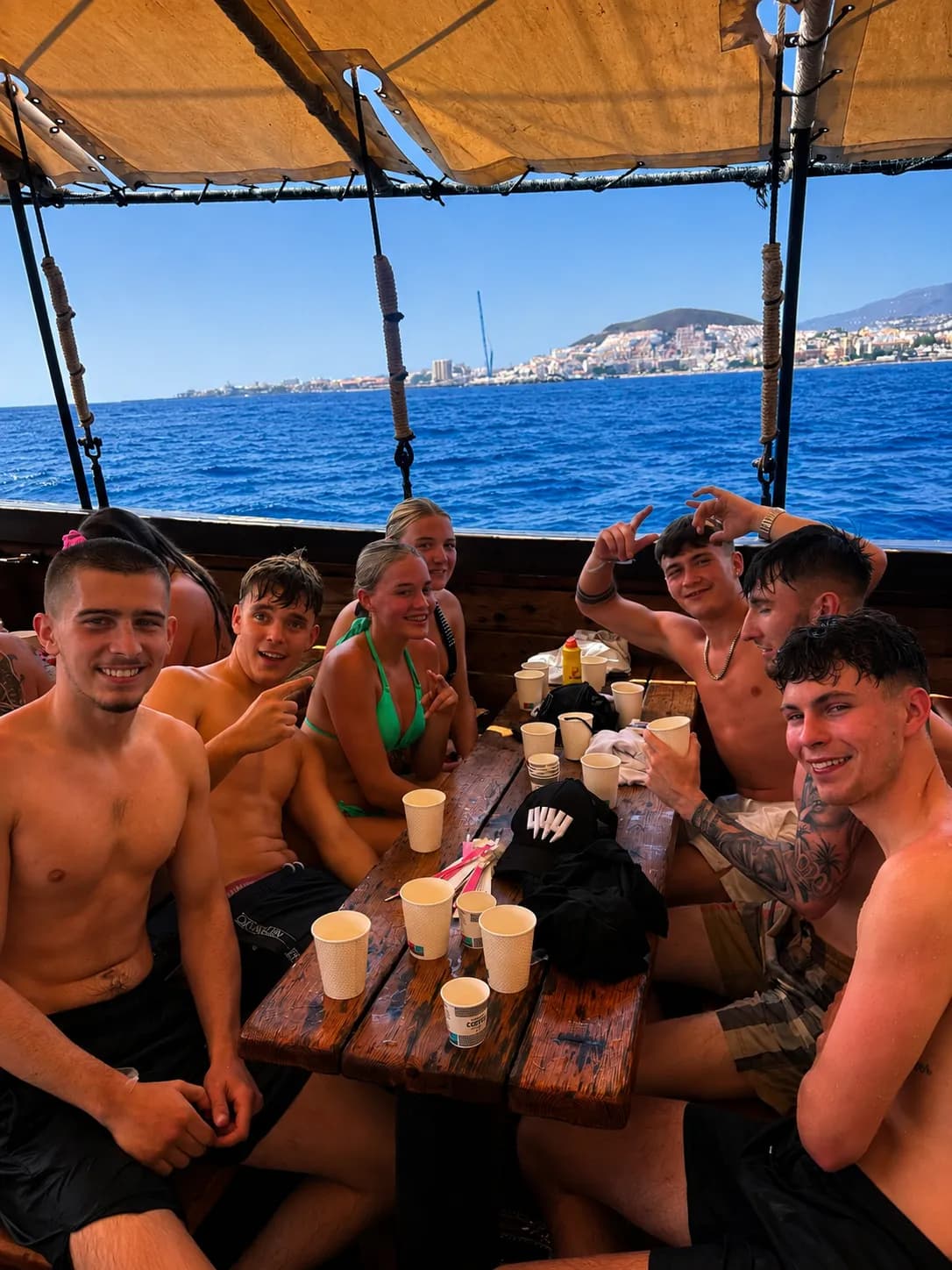 Group of young adults enjoying drinks on boat with coastal town view