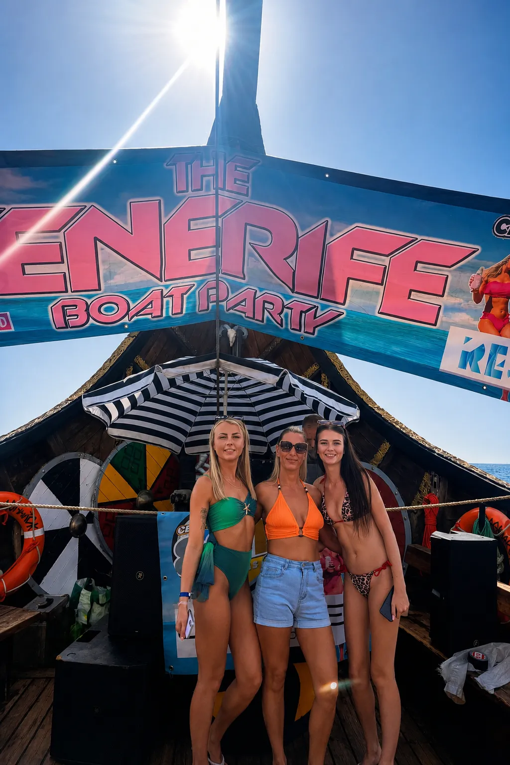 Three women posing under striped umbrella at Energee Boat Party