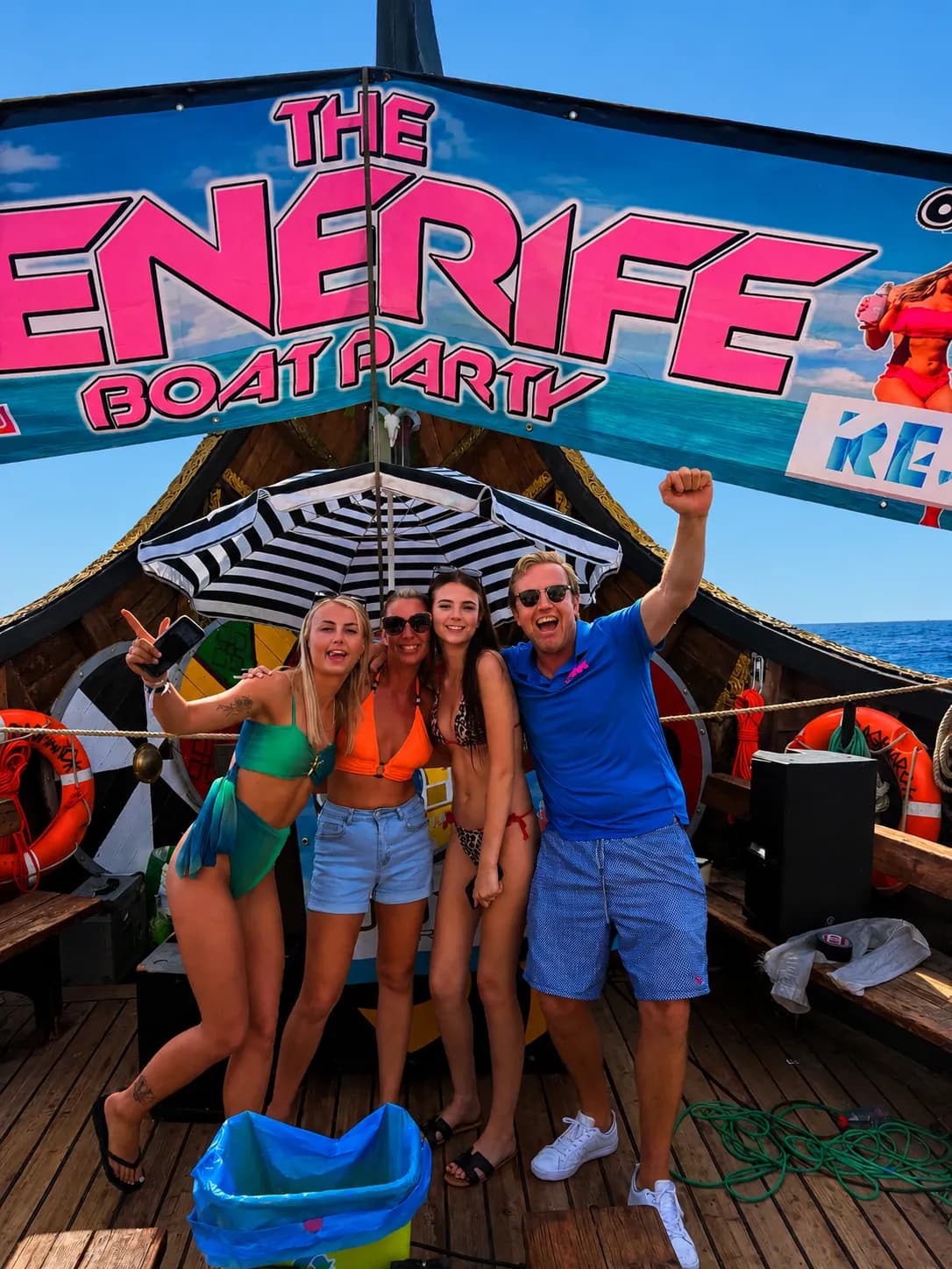 Four guests posing under striped umbrella on Energee boat party deck