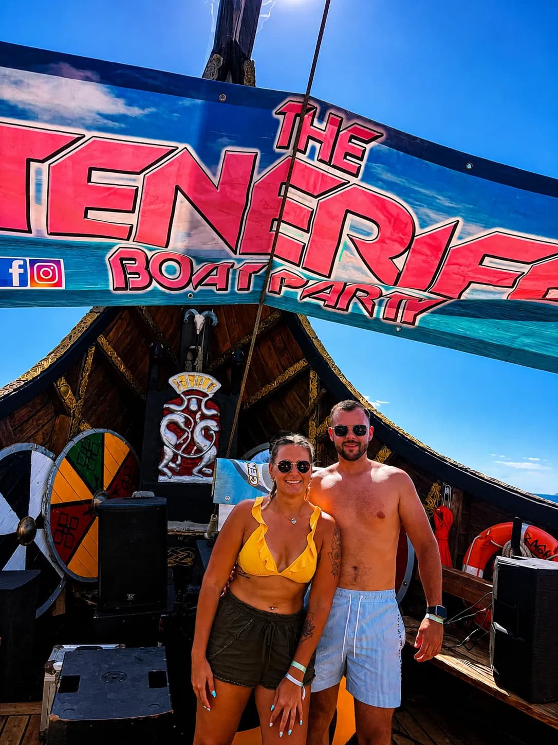 Two guests posing under The Generife boat party sign on deck